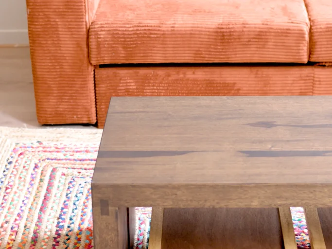 Table en bois foncé devant un canapé orange, sur un tapis coloré.