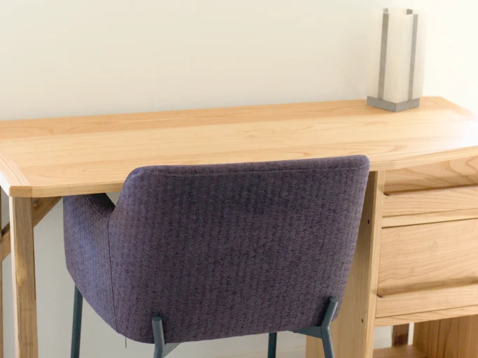Bureau en bois clair avec une chaise violette et une lampe sur le dessus.