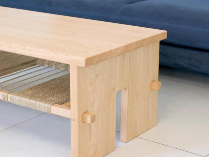 Table basse en bois clair avec étagère en dessous, situé près d'un canapé bleu.