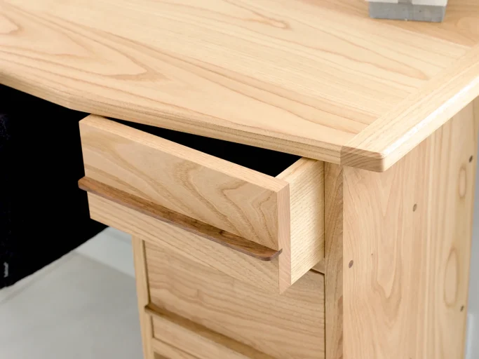 Tiroir en bois clair partiellement ouvert sur un bureau en bois naturel.